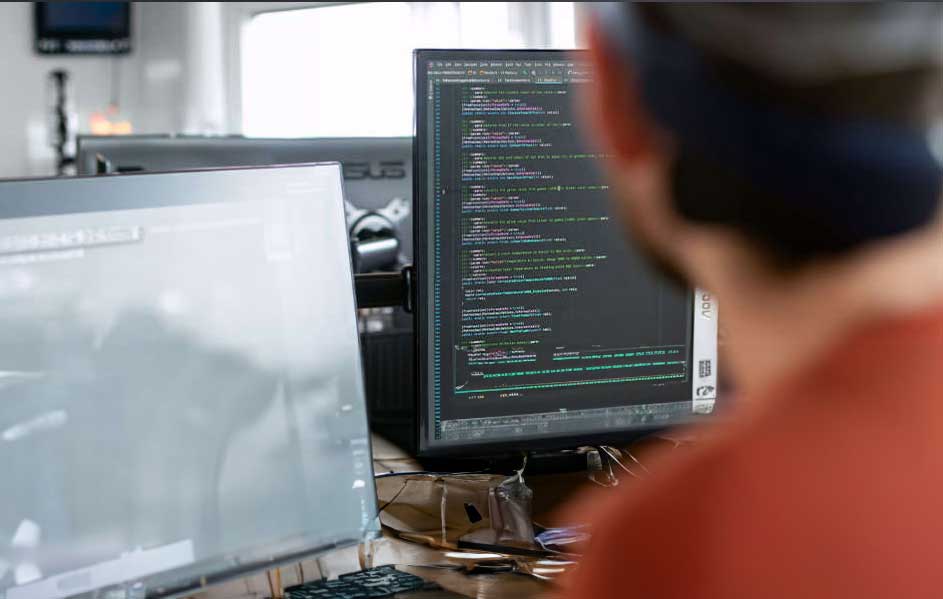 Un bureau avec deux écrans d'ordinateur affichant du code, un clavier et des lunettes. L'arrière-plan est flou.