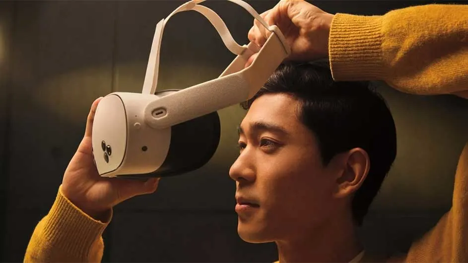 Een witte VR-bril wordt in de hand gehouden, terwijl iemand anders de band aanpast. De achtergrond is donker.