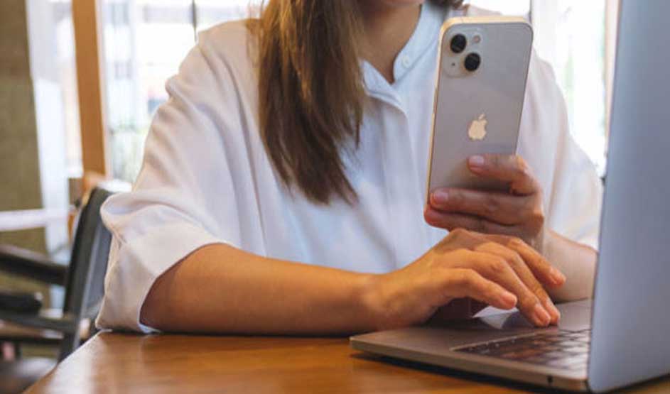 Une table en bois soutient un ordinateur portable gris ouvert et un smartphone argenté.