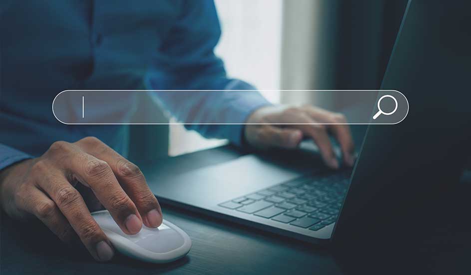Un ordinateur portable sombre avec une barre de recherche blanche est utilisé avec une souris blanche sur un bureau sombre.