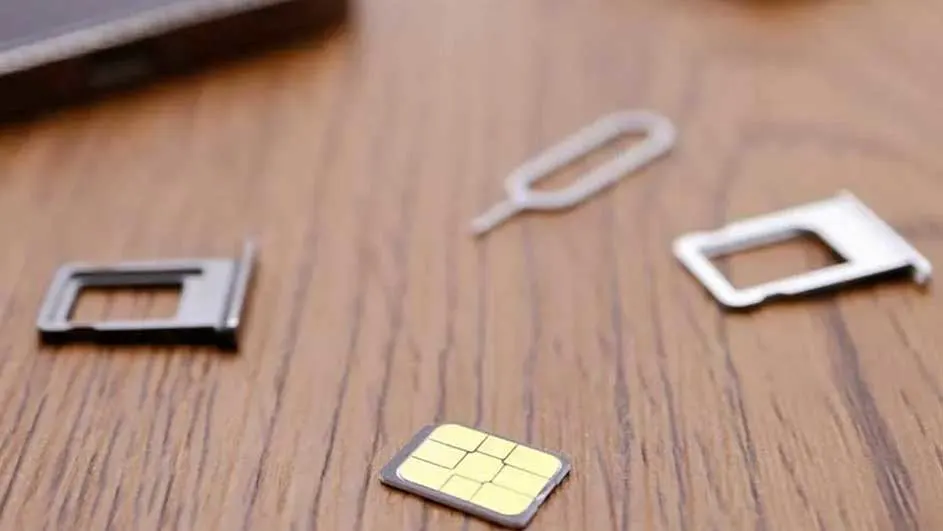 Sur une table en bois, une carte SIM jaune, deux supports SIM blancs et un outil d'éjection SIM blanc sont visibles.