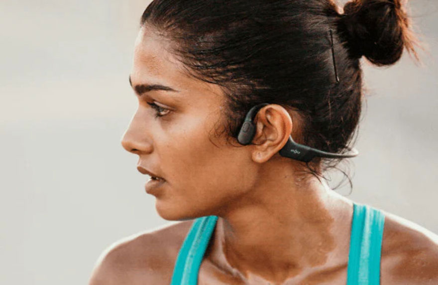 Een close-up van een persoon met een blauw topje en een zwarte hoofdtelefoon die over het oor is geplaatst.