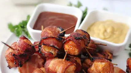 Gros plan d'une assiette de bouchées de poulet enroulées de bacon, fixées avec des cure-dents, avec des sauces à tremper.