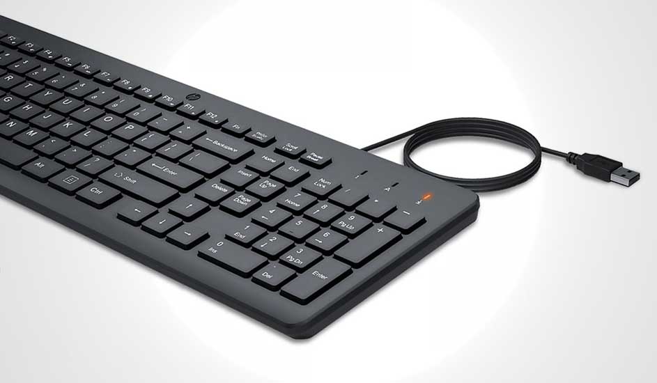 Clavier noir avec câble USB sur fond blanc. Le clavier est orienté en diagonale. Une lumière orange est visible.