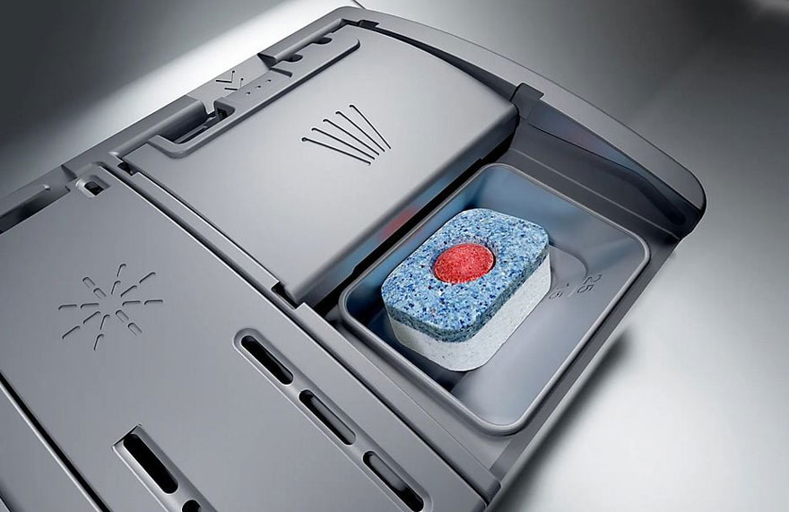 Un compartiment de lave-vaisselle gris contient une pastille bleu, blanche et rouge sur un fond gris.