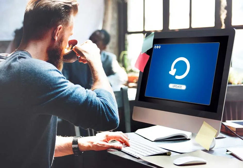Een computerscherm met een blauw scherm dat een update-pictogram toont, staat op een bureau met een toetsenbord en een muis.