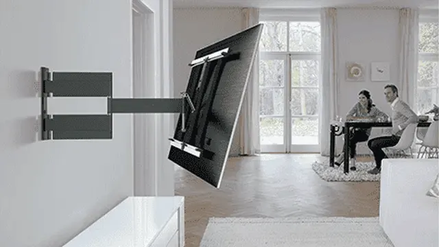 A wall-mounted, adjustable television bracket holds a black screen. In the background is a room with a table and a window.
