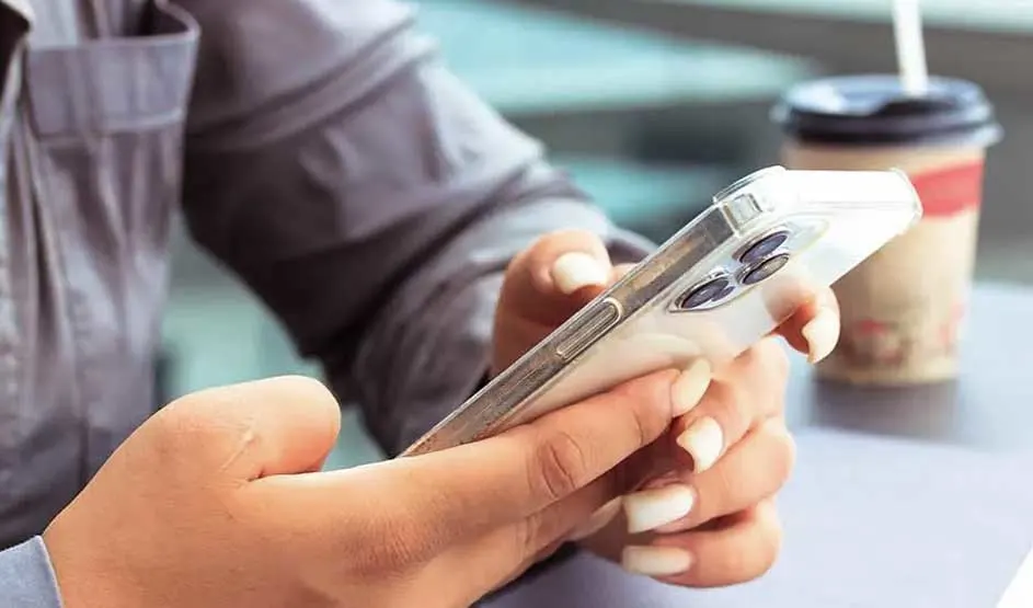 Une personne tient un iPhone Apple à trois caméras, gobelet de café à côté, ambiance décontractée, marque Apple présente.