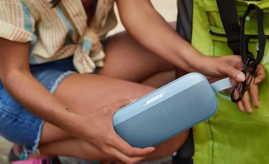 Enceinte bleue tenue à côté d'un sac à dos vert. L'enceinte porte le logo Bose.