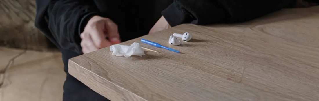 Une table en bois présente des écouteurs blancs, un outil bleu et un mouchoir en papier.