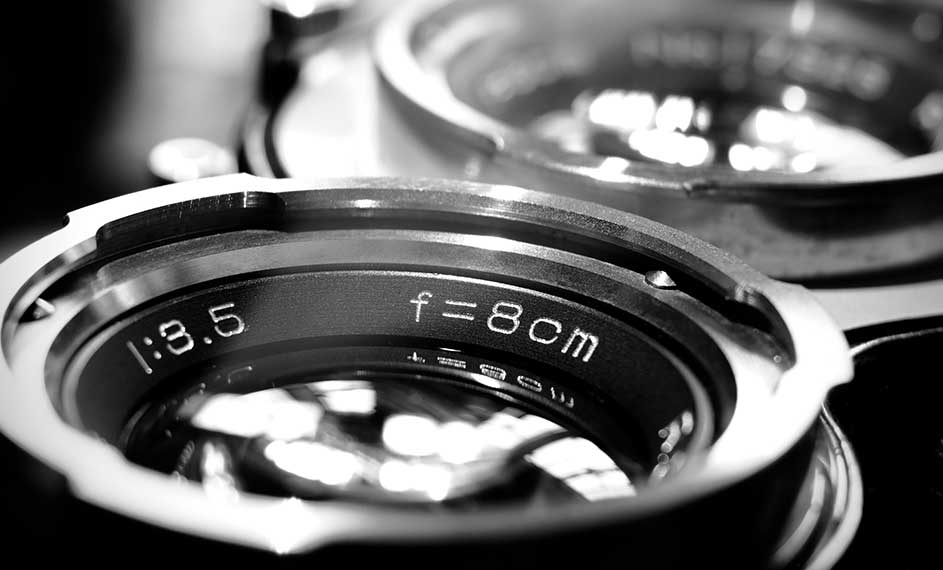 Gros plan en noir et blanc d'un objectif de caméra argentique avec les inscriptions "1:3.5" et "f=8cm" en blanc.