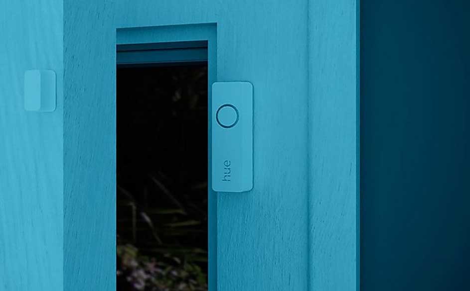 Een blauwe muur met een rechthoekige, blauwe 'hue' schakelaar en een doorkijk naar buiten.