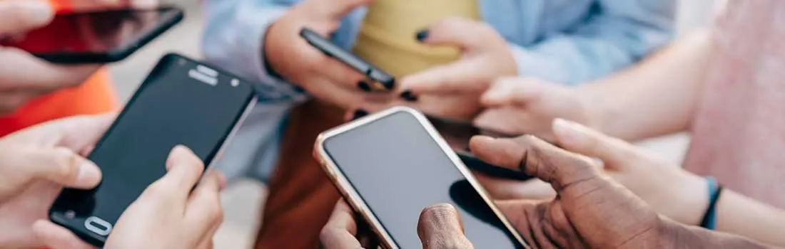 Multiple hands hold various smartphones, some with black cases, others gold, against a backdrop of colorful clothing.