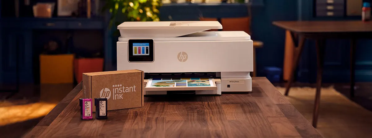 Imprimante HP sur une table en bois avec une boîte HP Instant Ink et des cartouches devant.