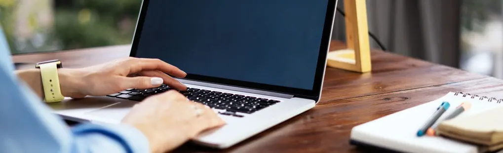 Laptop on a wooden desk with a notebook, pen, and a wooden frame.