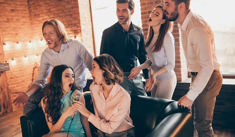Een groep mensen zingt karaoke in een kamer met bakstenen muren en lichten. Er is een microfoon zichtbaar.