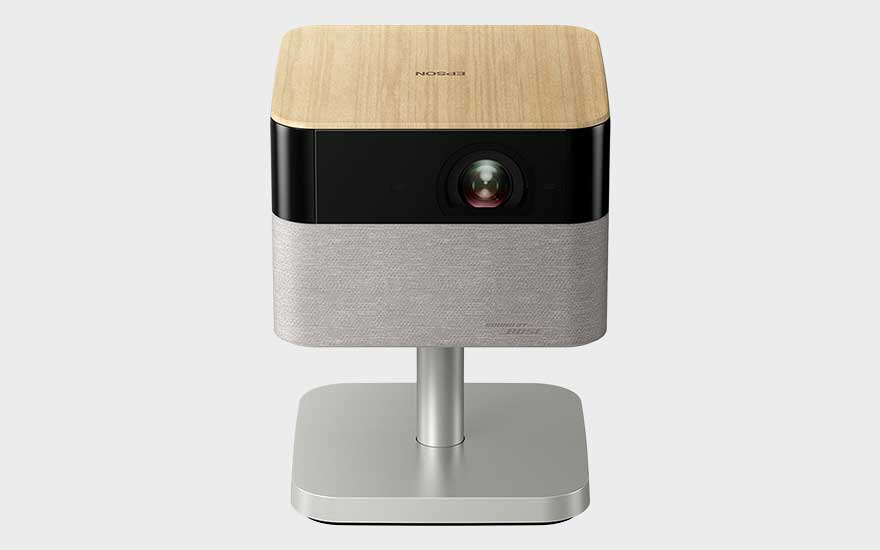 Projecteur Epson compact sur pied argenté, avec dessus en bois, zone de lentille noire et finition claire en tissu.