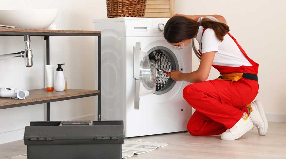 Een witte wasmachine staat in een badkamer naast een houten rek en een grijze gereedschapskist.