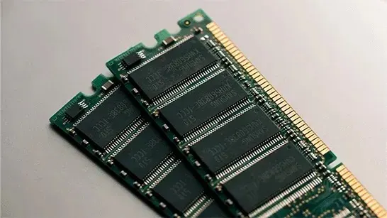 Two green RAM sticks rest at an angle on a pale surface, showing black memory chips and a row of gold contacts.