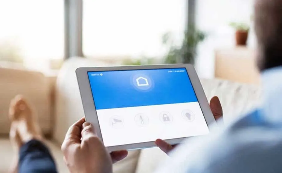 Een tablet toont een blauw en wit scherm met een huisicoon. De tablet wordt vastgehouden in een interieur.