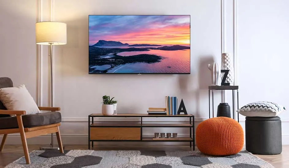 Une TV LG est fixée au mur dans un salon élégant avec meuble en bois, pouf orange et accessoires décoratifs.