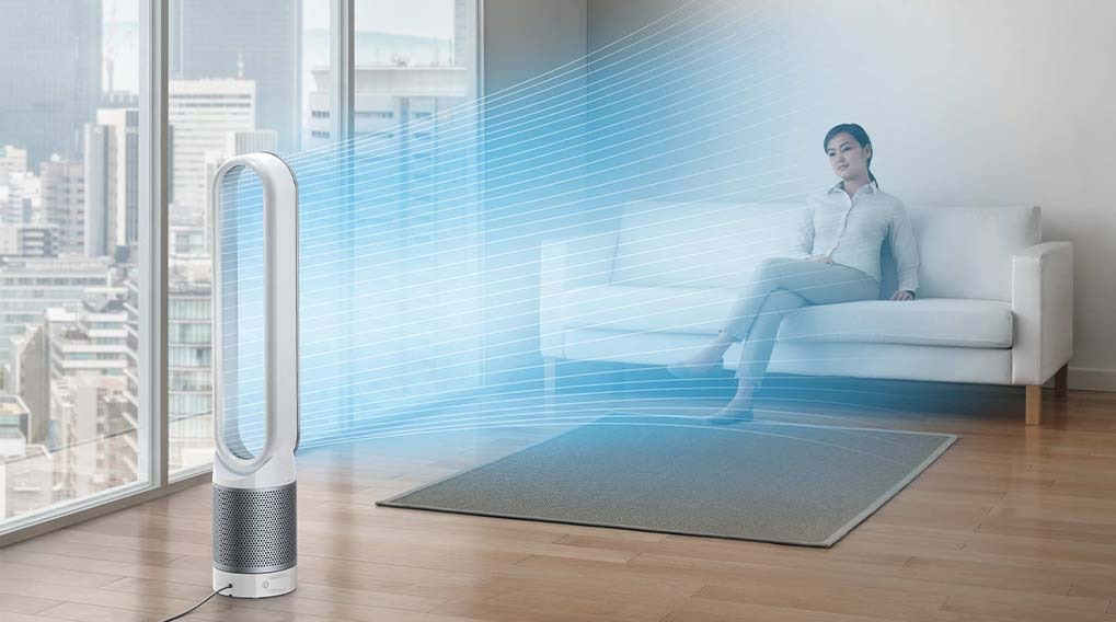 Witte ventilator blaast blauwe lucht in een kamer met houten vloer, een grijs tapijt en een witte sofa. Buiten het raam staan hoge gebouwen.