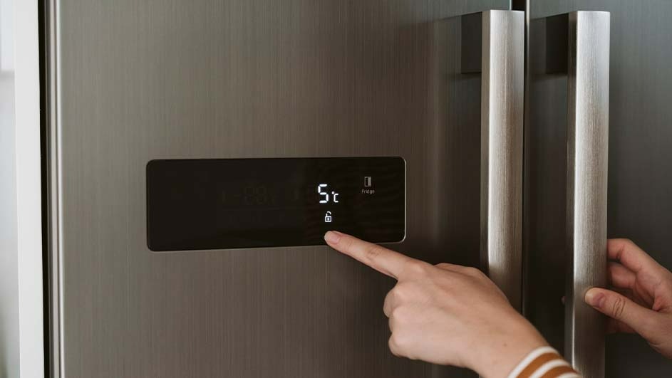 Metalen koelkast met handgrepen en digitaal scherm dat 5°C en een slotpictogram toont; een vinger raakt het scherm aan.