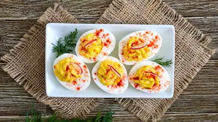 Cinq œufs mimosas farcis sur assiette blanche, paprika, herbes. Nappe en jute sur table en bois.