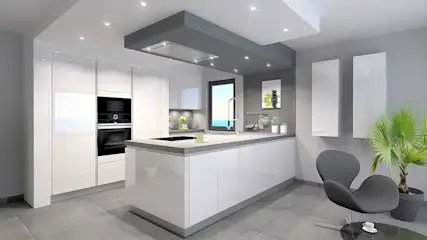 Cuisine moderne avec armoires blanches, îlot central, plan de travail gris et sol carrelé. Une chaise grise et une plante sont visibles.