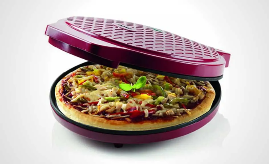 Een rode pizzaoven staat open met een pizza erin. De pizza heeft toppings zoals kaas, groenten en kruiden. De achtergrond is wit.