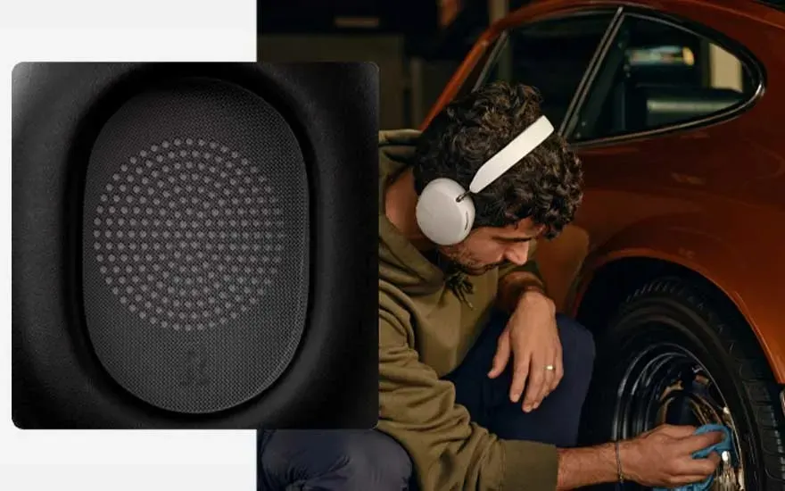 Un casque audio noir avec une grille intérieure est présenté à côté d'une voiture orange, où quelqu'un nettoie les pneus.