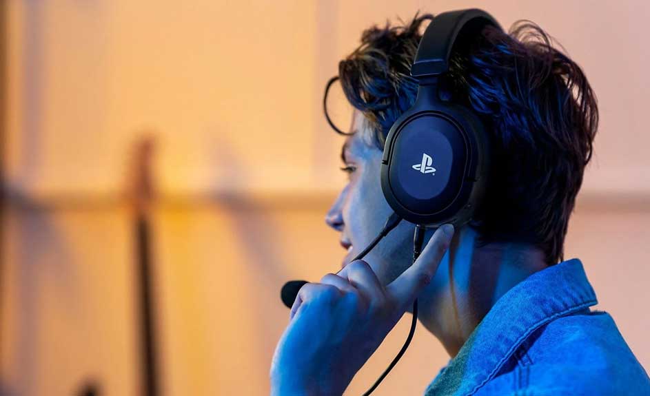 Een zwarte gaming headset met microfoon, blauwe accenten en een PlayStation logo. Het heeft een zwarte kabel. Op de achtergrond een vage oranje muur.