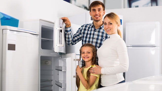 Un réfrigérateur blanc avec porte ouverte est présenté dans un magasin d'électroménager avec d'autres appareils blancs.