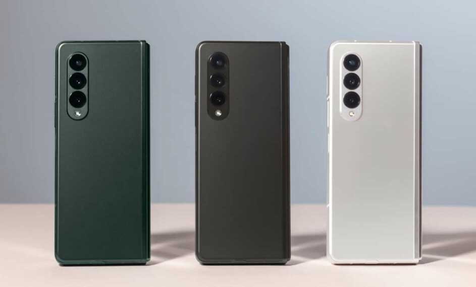 Trois téléphones pliables vert, gris et blanc avec trois objectifs de caméra sont alignés sur une surface claire.