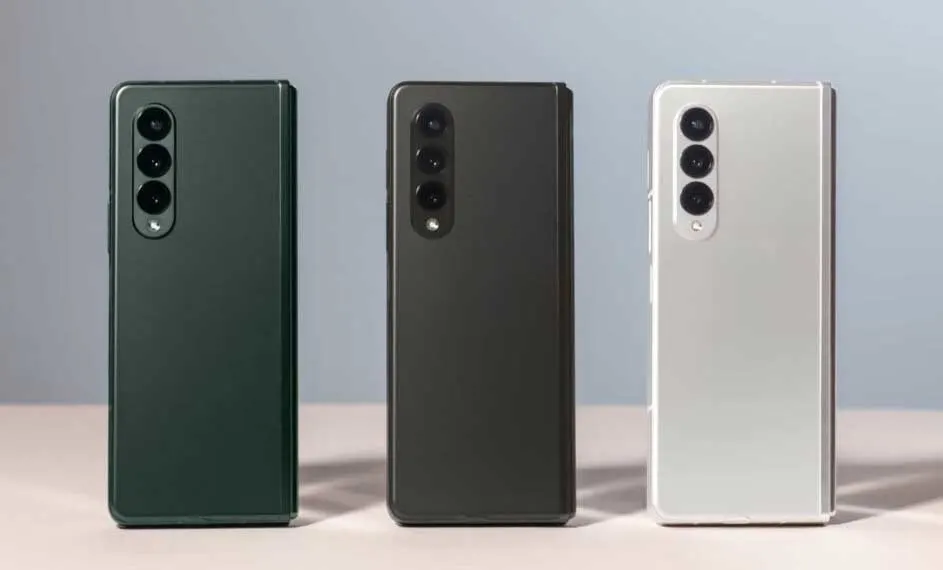Drie smartphones in groen, grijs en wit staan rechtop, met drie camera's aan de achterkant.