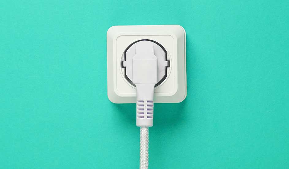 Een witte stekker in een wit stopcontact tegen een turquoise achtergrond.