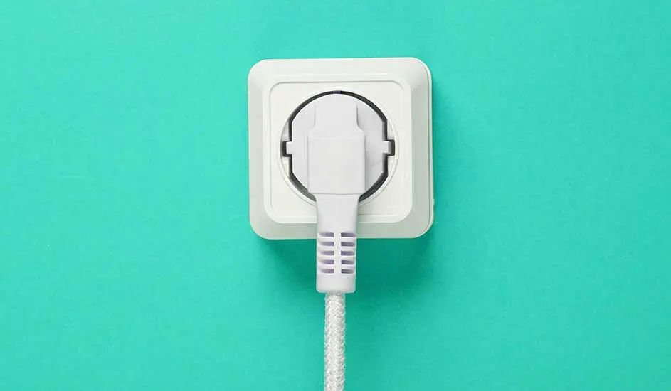 Een witte stekker in een wit stopcontact tegen een turquoise achtergrond.