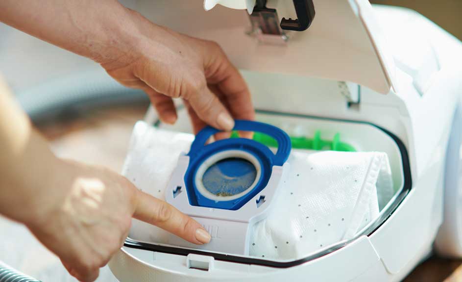 Handen vervangen een stofzak in een witte stofzuiger. De stofzak heeft een blauwe rand.