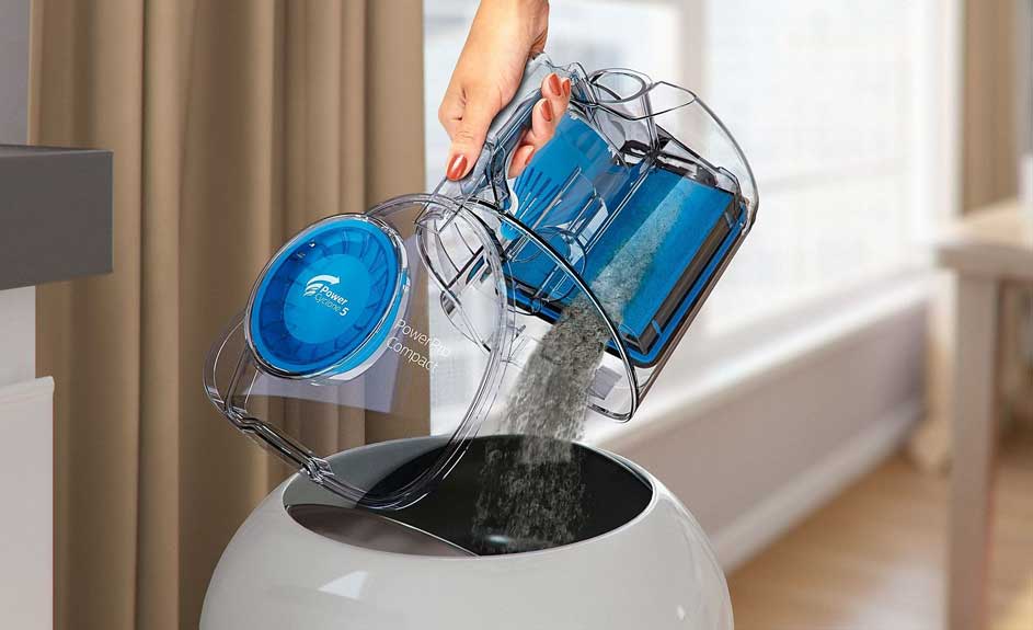 Réservoir d'aspirateur transparent vidé dans une poubelle blanche. Le filtre bleu est visible.