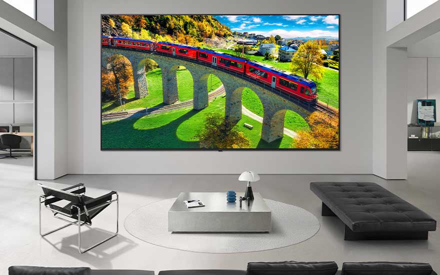 Une grande télévision dans un intérieur spacieux montre un train rouge sur un viaduc dans un paysage vert.