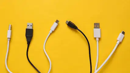 Zes USB-kabels (wit en zwart) liggen op een gele achtergrond. Er zijn verschillende types connectoren te zien.