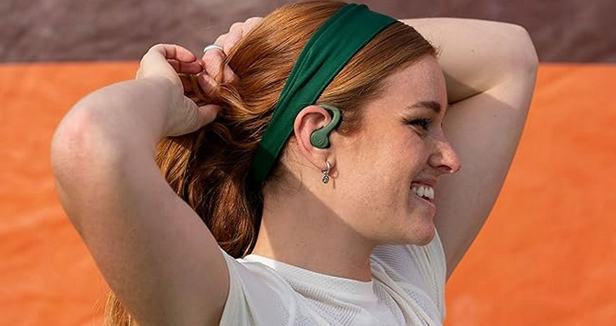 Een vrouw met een groene hoofdband en oortelefoon staat voor een oranje achtergrond.
