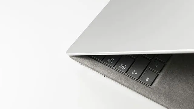 Vue rapprochée d'un ordinateur portable argenté partiellement ouvert sur un fond blanc. Le clavier noir est visible.