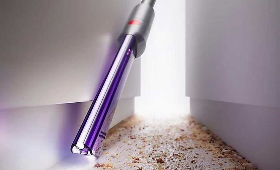 Aspirateur violet et gris près des miettes sur une surface blanche, avec un arrière-plan blanc flou.