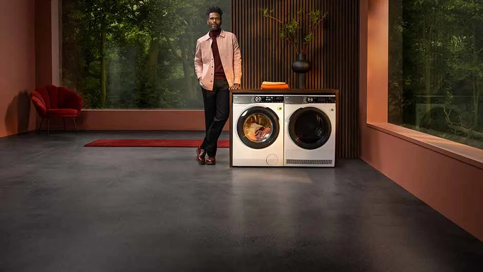 Wasmachines staan in een kamer met houten lambrisering en een groot raam met uitzicht op bomen.