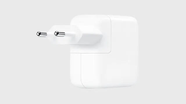 Un adaptateur secteur blanc avec deux broches métalliques sortant, sur fond gris clair.