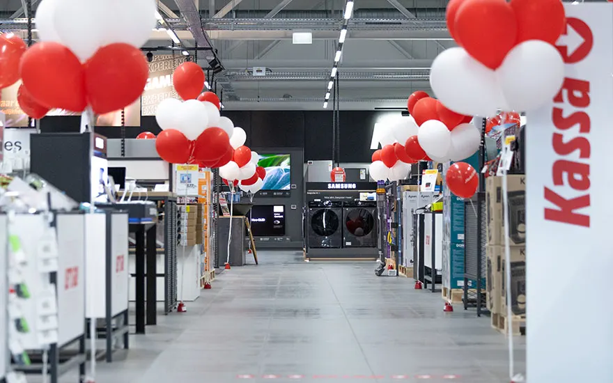 Binnenkant MediaMarkt winkel met rode en witte ballonnen die de gangpaden versieren. Schone, moderne winkelruimte klaar.