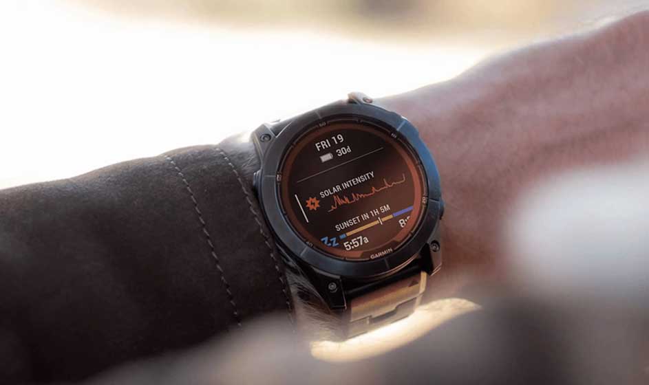 Une montre connectée noire et sportive est portée au poignet, au-dessus d’une manche sombre. Son écran rond affiche plusieurs données liées au sport et à la santé.
