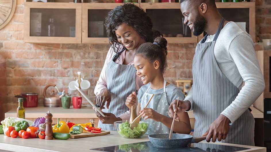 Une cuisine avec des légumes frais sur un comptoir, des ustensiles de cuisine et une famille en train de cuisiner.