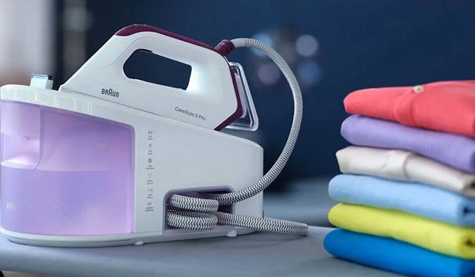 Een wit Braun stoomstrijkijzer staat naast een stapel gekleurde kleding op een grijze ondergrond, tegen een blauwe achtergrond.